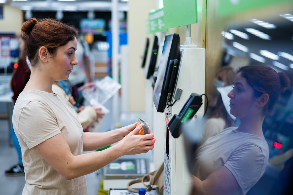 Mulher realizando autoatendimento em terminal de pagamento em supermercado, ilustrando tendencias em autoadesivos e RFID no varejo.