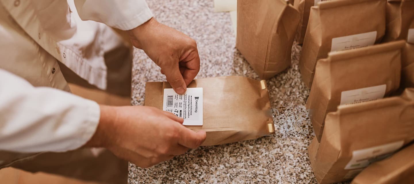 Hands affixing a thermal paper label to a brown paper bag.