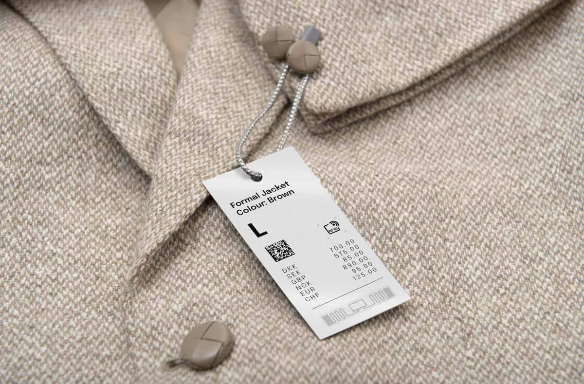 Etiqueta RFID para controle de estoque em tag de roupa pendurada em jaqueta marrom, com tamanho L, QR code e símbolo RFID.