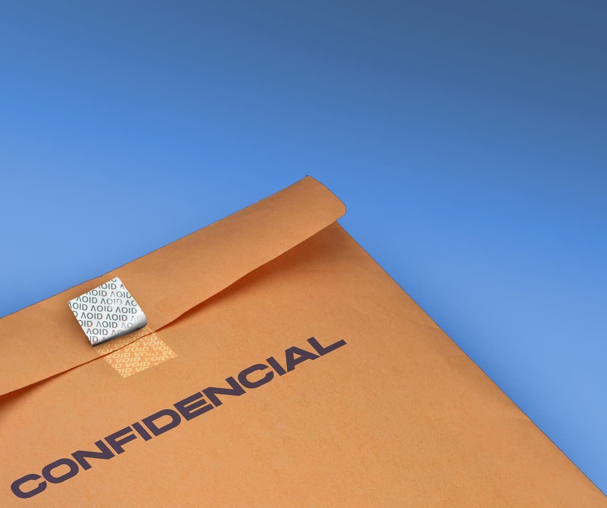 Sobre marrón confidencial con una etiqueta VOID de seguridad parcialmente retirada, sobre fondo azul.
