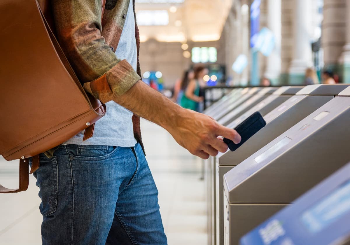 Persona utilizando un smartphone en un lector de acceso en una estación, ilustrando el uso de tecnología sin contacto con etiqueta NFC para validación rápida y segura.