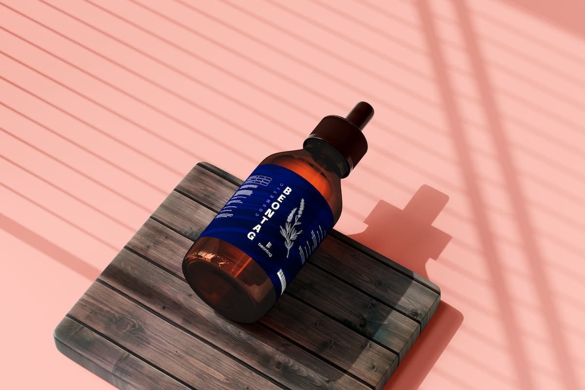 Amber dropper bottle with a blue label resting on a wooden board against a pink background with shadow lines.