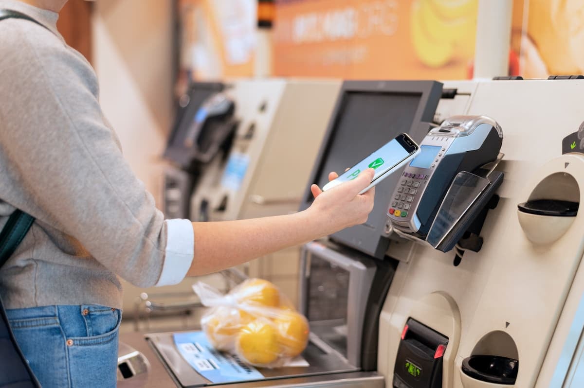 Customer using a smartphone with NFCtag technology to make a contactless payment at a self-checkout terminal.