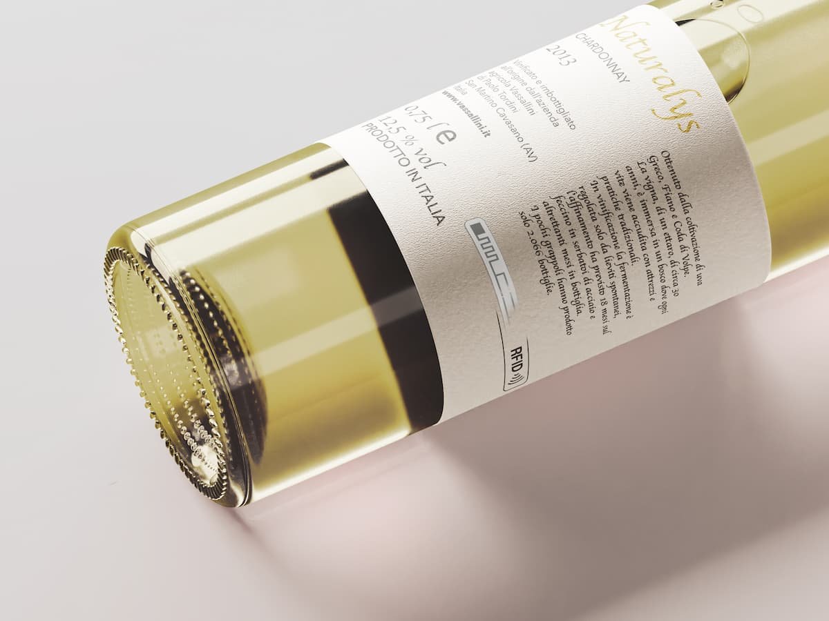 Close-up of a white wine bottle lying on its side, featuring a detailed label with product information and an RFID symbol, against a clean, neutral background.