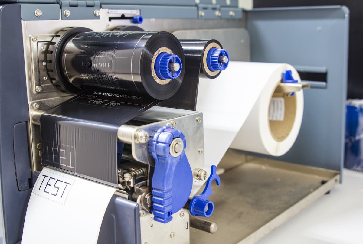 Thermal paper roll and black ribbon installed in a label printer mechanism.