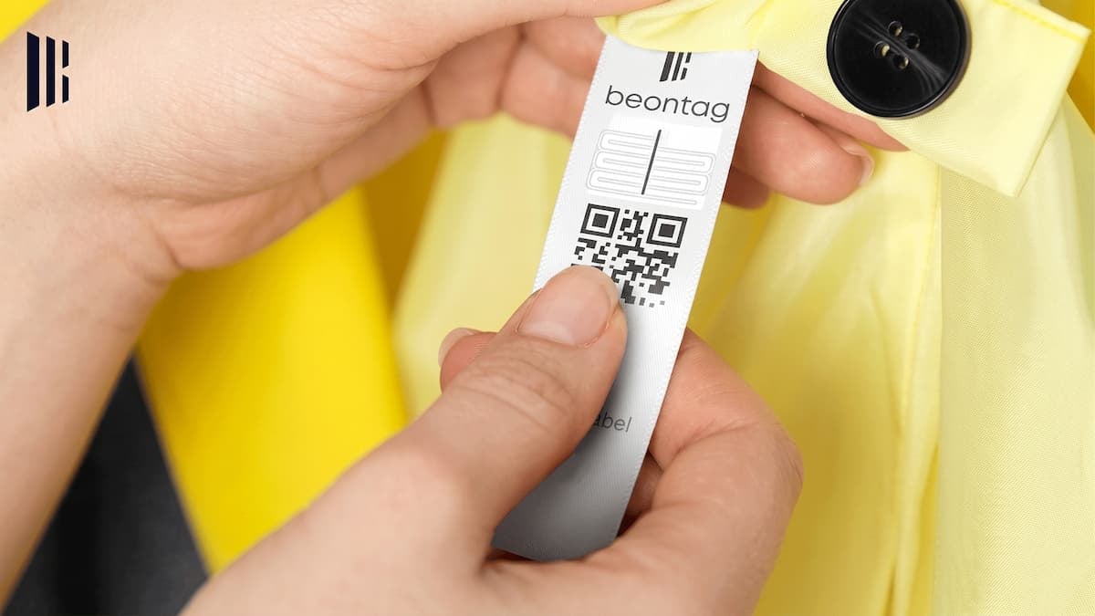 Close-up of hands holding a clothing tag with RFID technology and a QR code attached to a yellow garment, highlighting smart apparel tracking and product identification solutions.