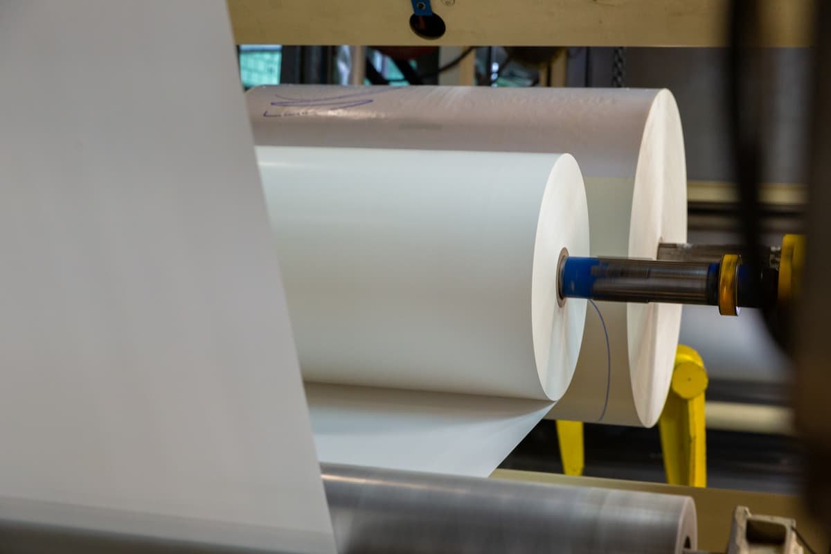 How to choose pressure-sensitive adhesive: large rolls of release liner material running through converting equipment in a production line.
